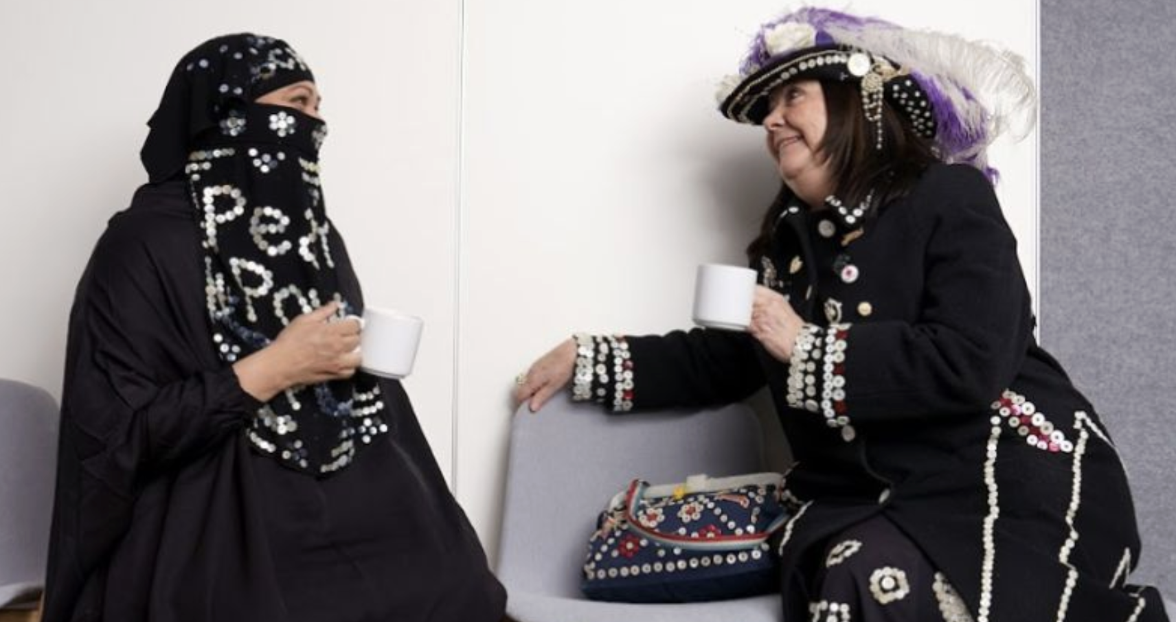Two women in distinctive traditional outfits sharing a conversation over tea, a warm and human photograph